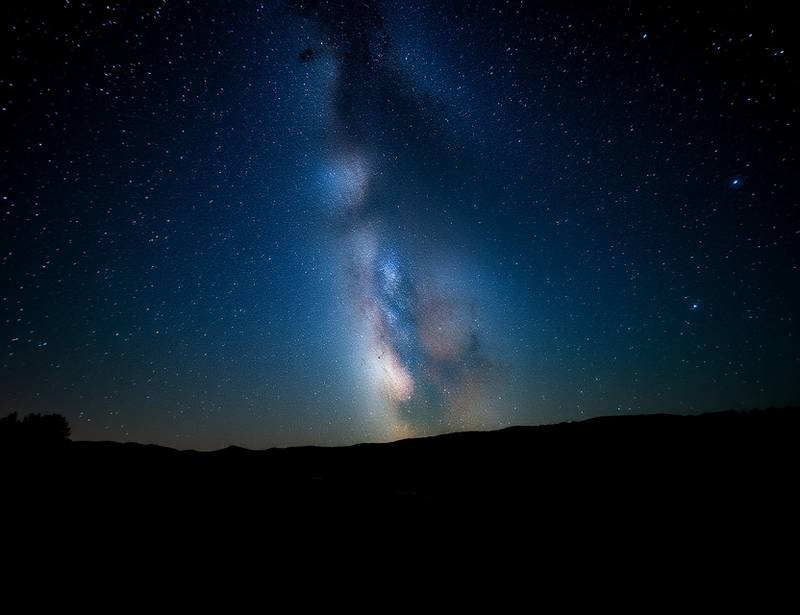 A photograph of a Milky Way over a dark landscape, illustrating astrophotography techniques.
